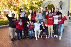 A group of students wave for a picture at the Sample Gates.